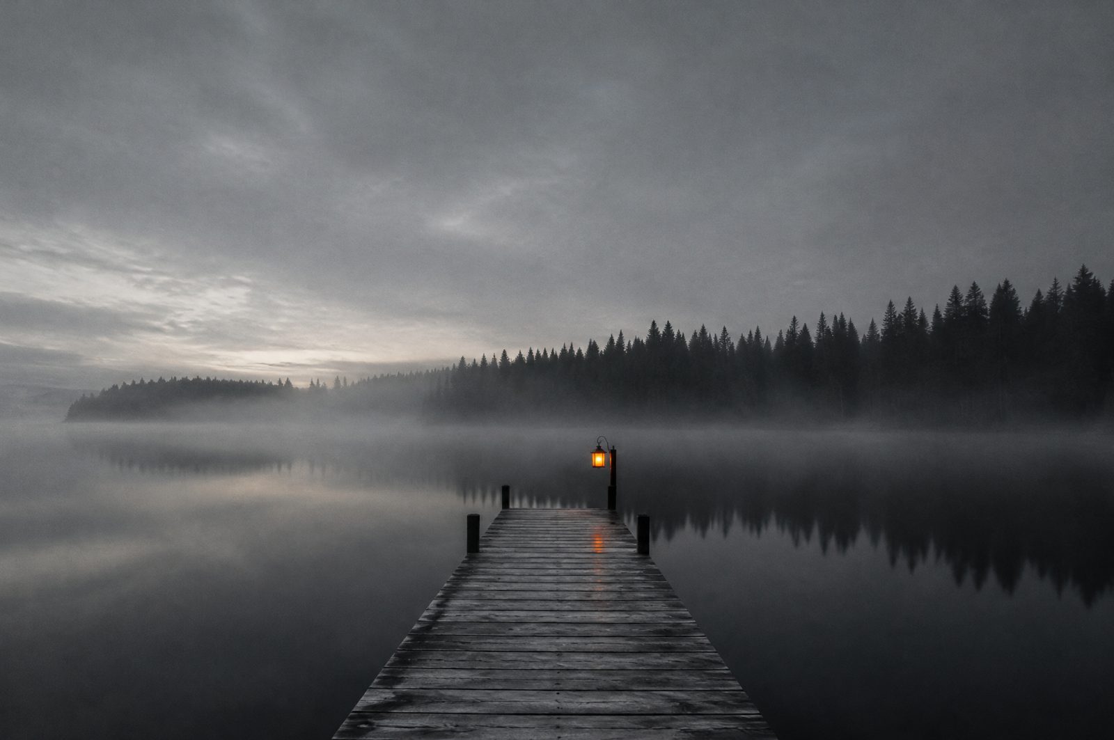 A wooden dock on a still lake at dawn with a single lantern lit